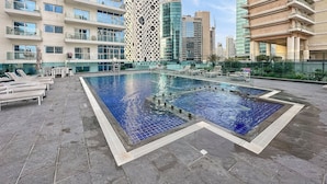 A rooftop pool area with lounge chairs and a distinctive building with circular cutouts. - Silkhaus Goldcrest Executive (Dubai)