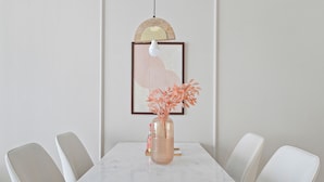 A dining table with a vase of orange flowers, surrounded by white chairs. - Silkhaus Goldcrest Executive (Dubai)