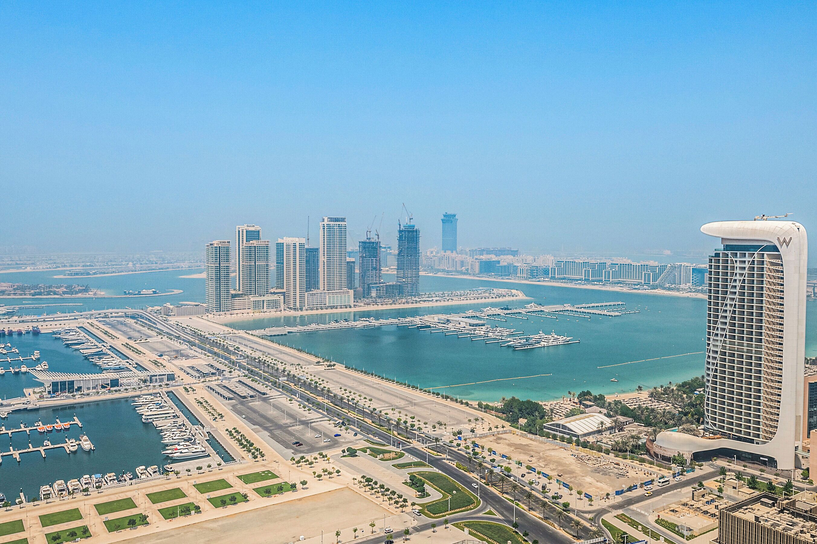 A marina with boats, a marina building, and several high-rise buildings in the background.