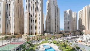Een hoog appartementencomplex met meerdere torens, een binnentuin met zwembad en een tennisbaan.