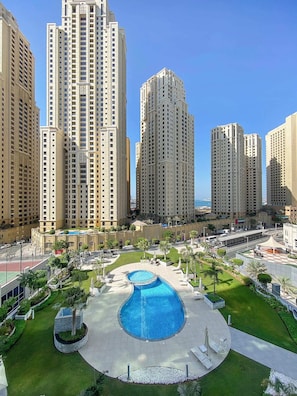 A high-rise residential building complex with a central swimming pool surrounded by greenery and a paved walkway.