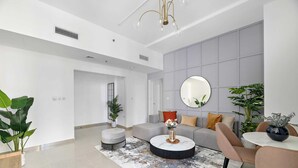 Een moderne woonkamer met een grijze bank, een rond bijzettafeltje en een grote spiegel.