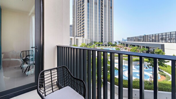 A balcony with a view of tall buildings, a swimming pool, and a chair.