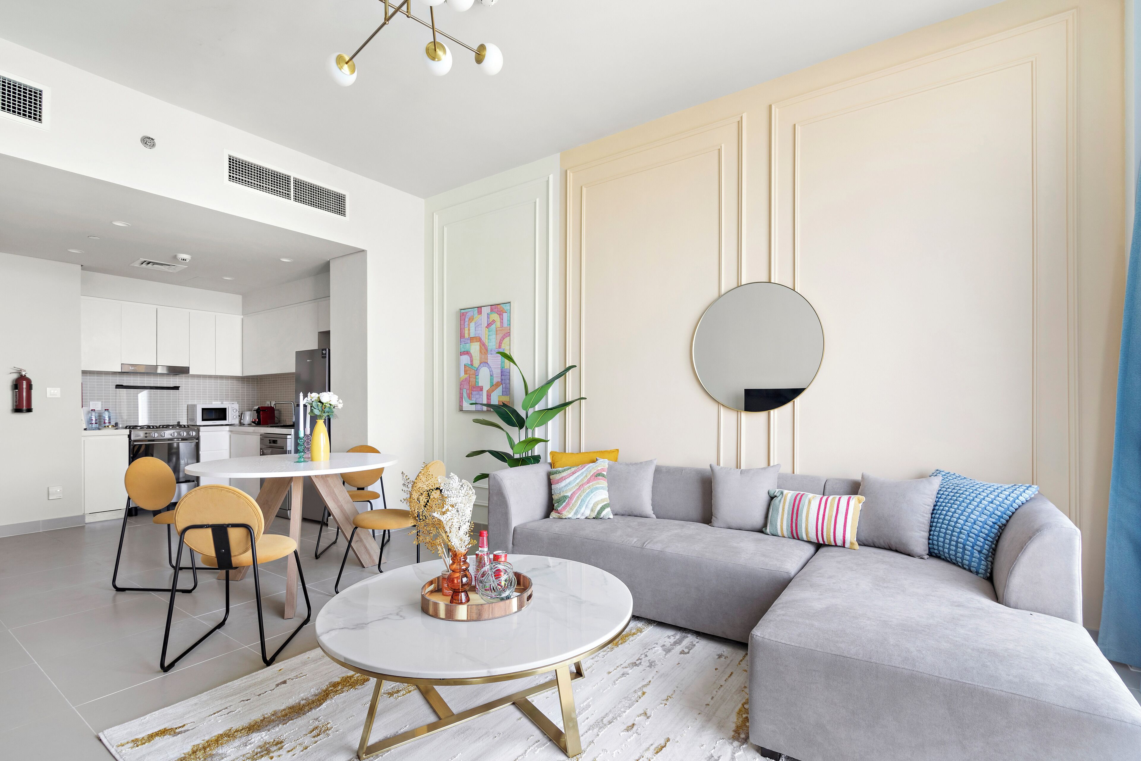 Un salon moderne avec un canapé d’angle gris, une table basse ronde et un coin repas avec des chaises jaunes.