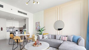 A modern living room with a grey sectional sofa, a round coffee table, and a dining area with yellow chairs.