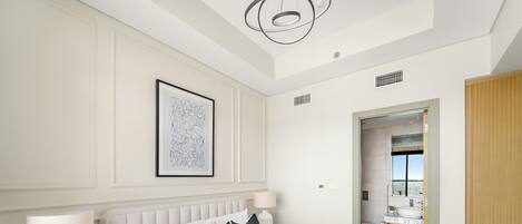 A modern hotel room with a large bed, white bedding, a framed artwork on the wall, and a view of the bathroom through an open door.