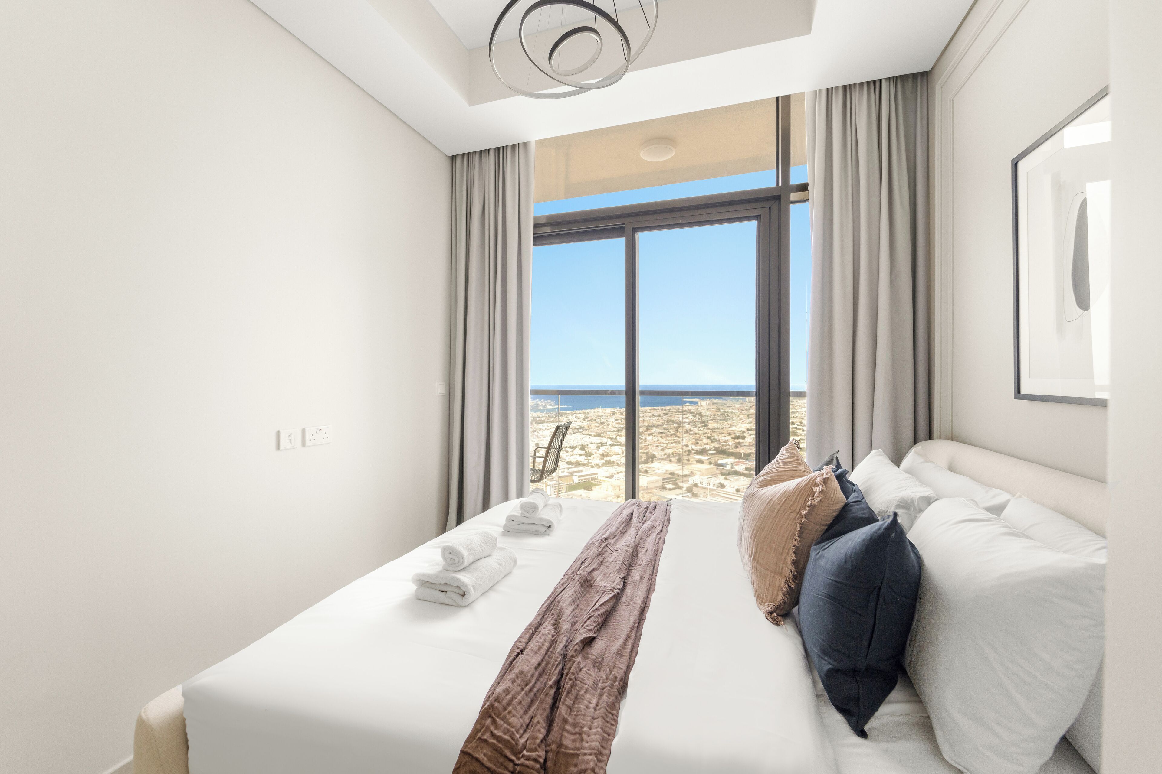 A hotel room with a large bed, a view of the beach, and a modern ceiling light.