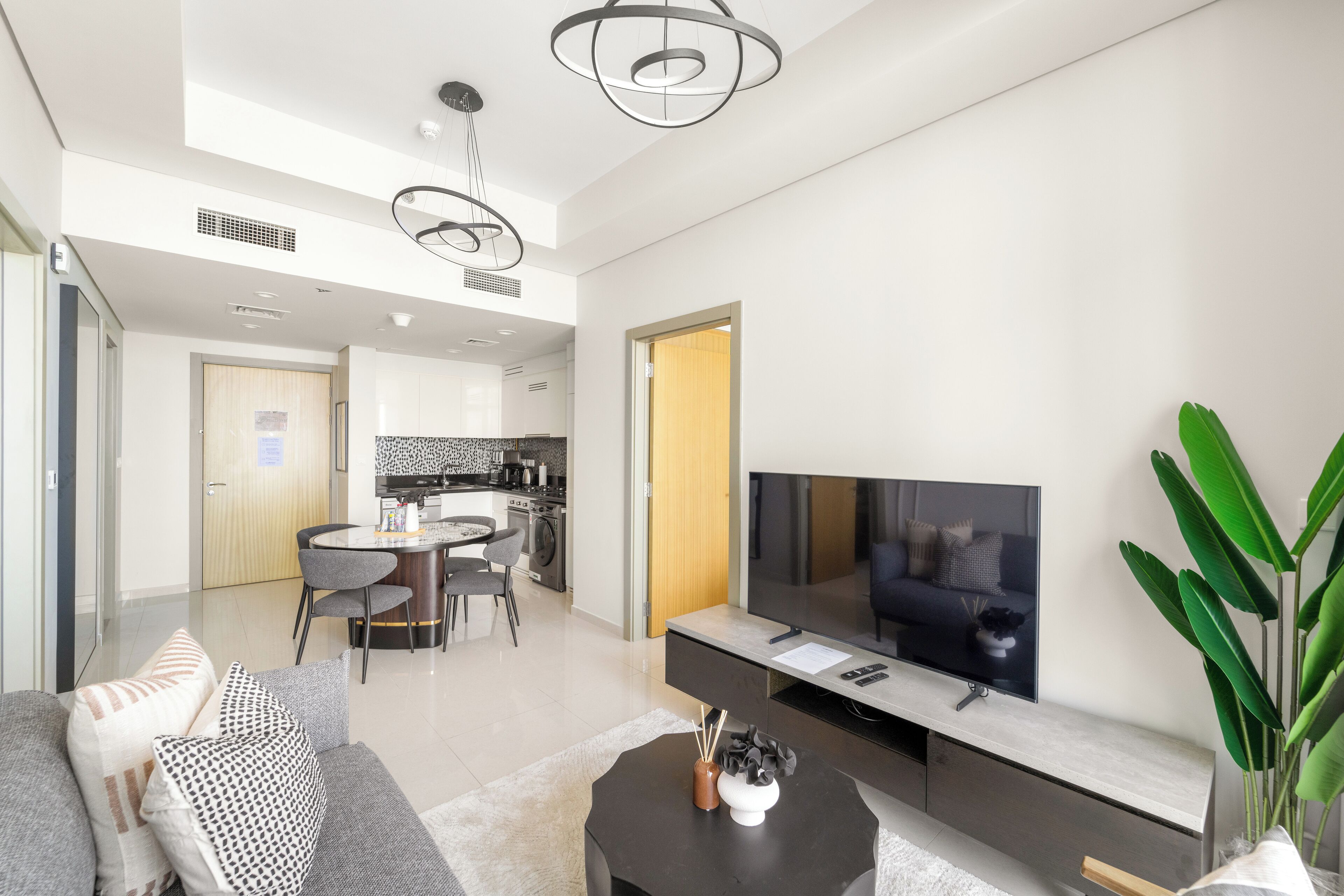A modern living room with a sofa, TV, and a dining area with chairs and a table.