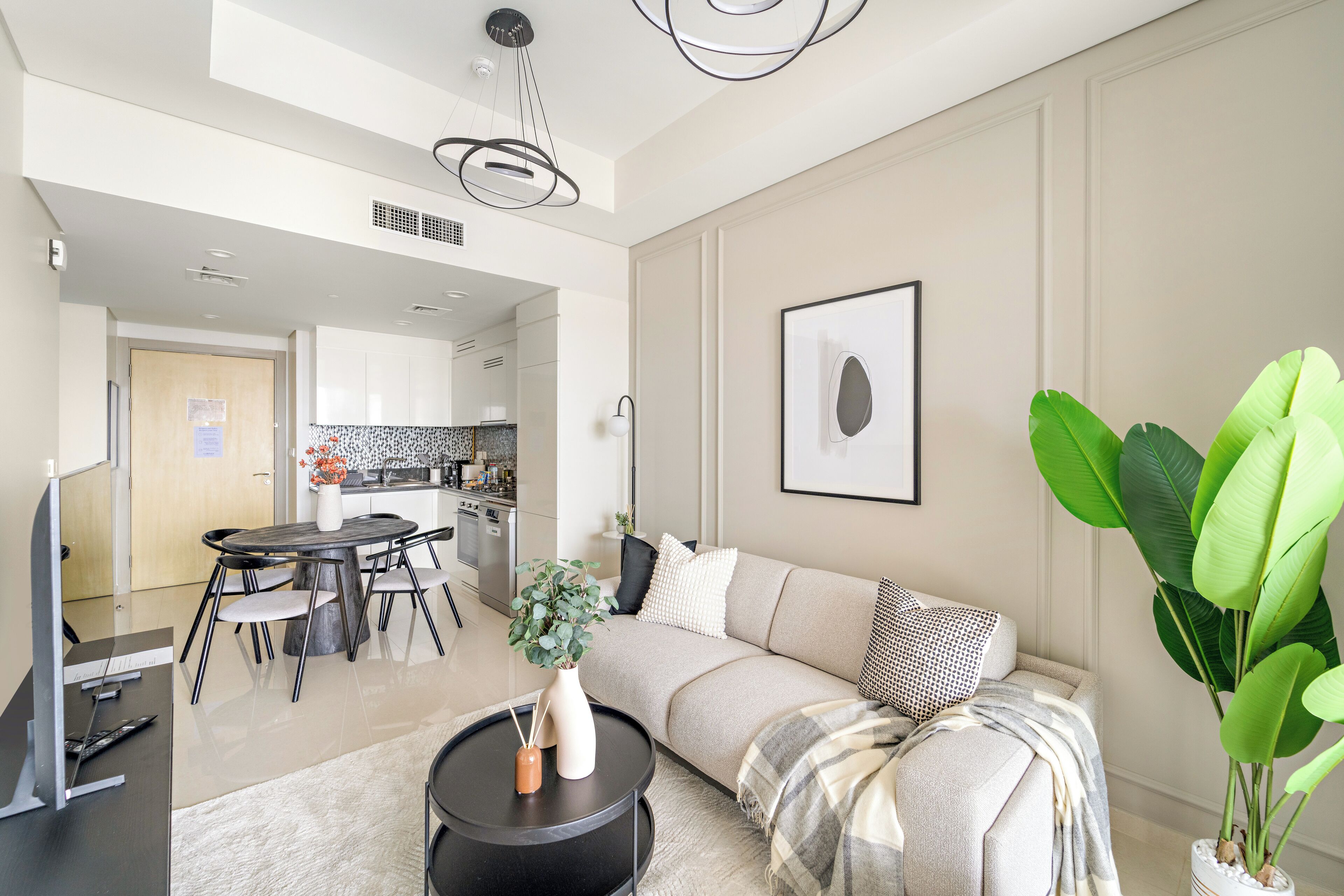 A modern living room with a sofa, a dining table, and a coffee table. There is a kitchen in the background.