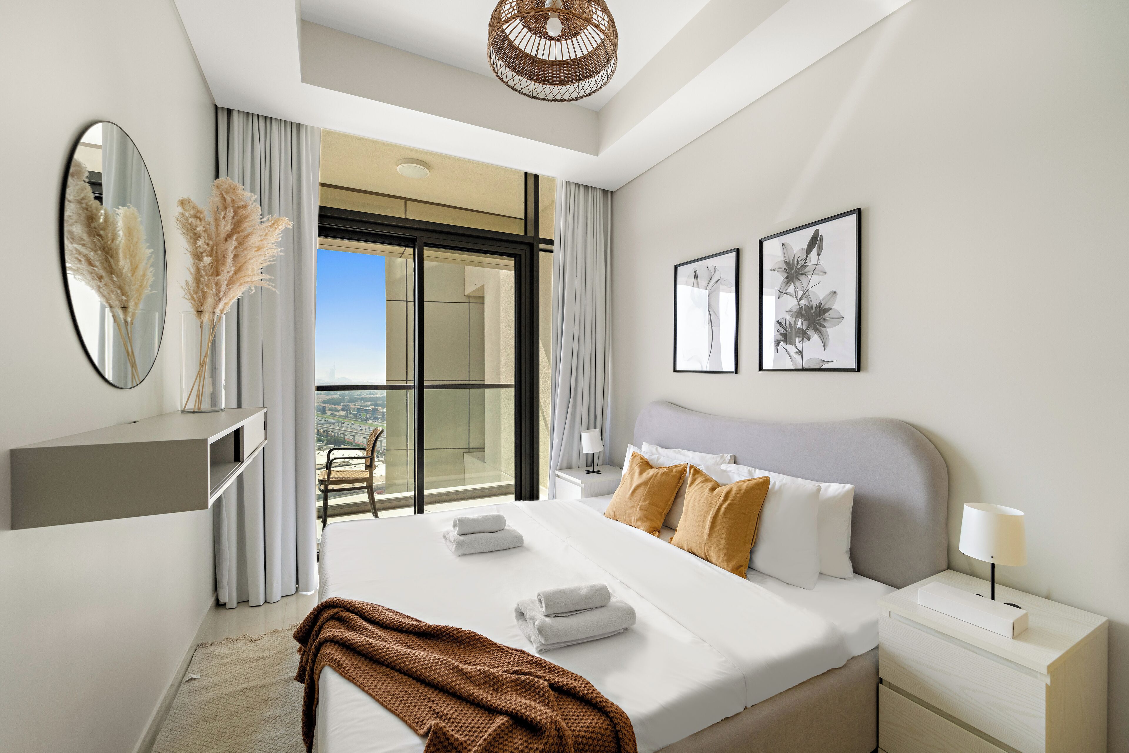 Une chambre d’hôtel moderne dotée d’un grand lit, d’une table de chevet avec une lampe, d’une vue sur la ville grâce à une grande fenêtre et d’un balcon.