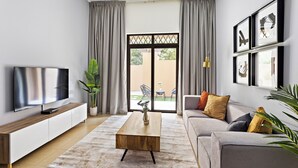 Una sala de estar moderna con un televisor de pantalla plana, una mesa de centro de madera, un sofá gris y un ventanal con cortinas.
