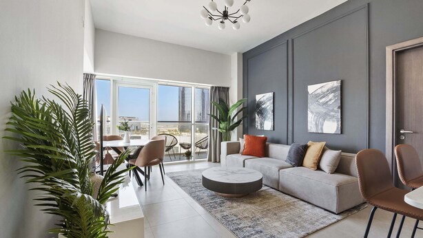 A modern living room with a grey sofa, round coffee table, and a large window offering a city view. - Silkhaus Marina Rise Towers (Abu Dhabi)