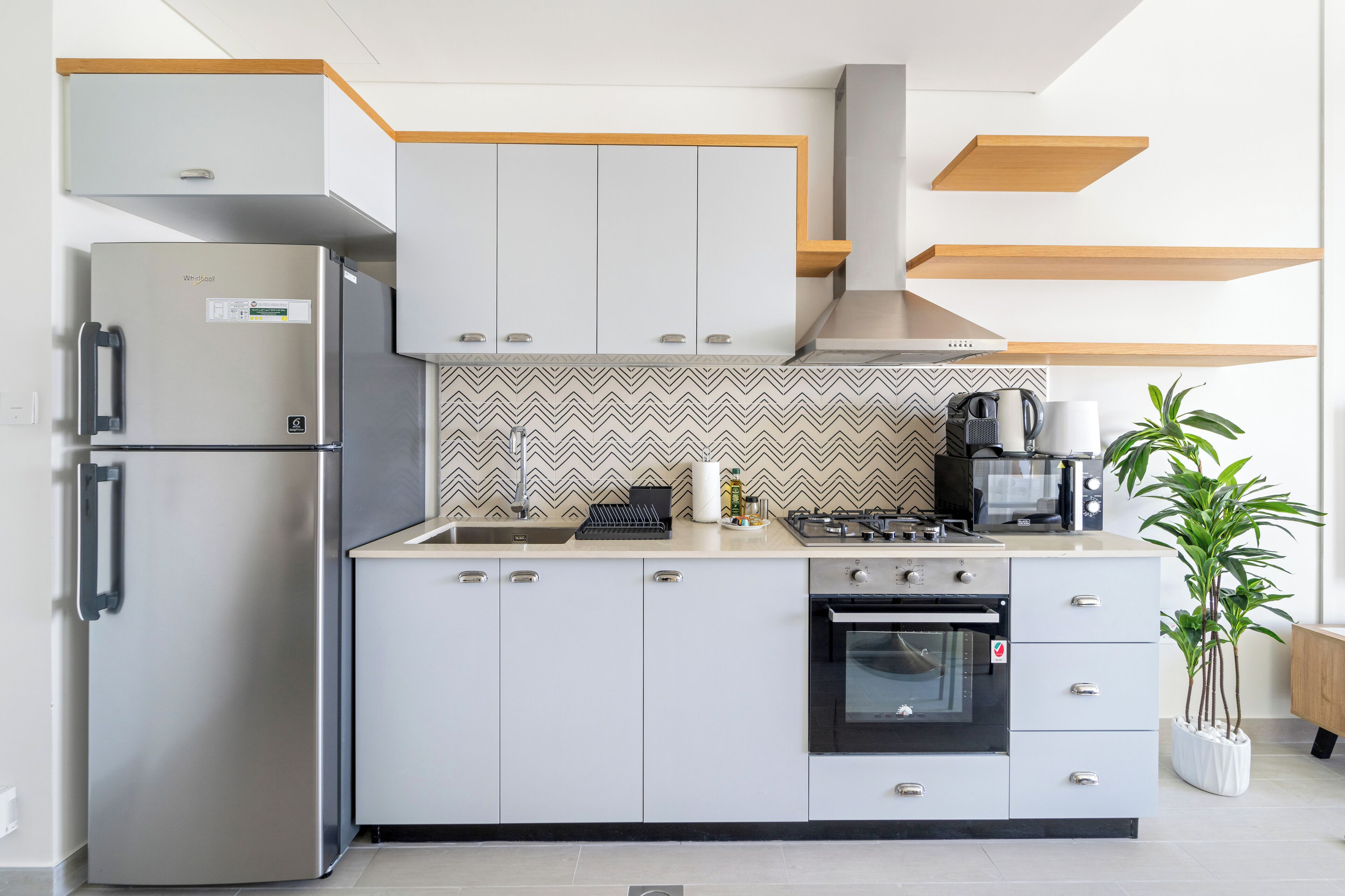 A modern kitchen with a built-in refrigerator, stove, oven, and microwave. There is a sink and a potted plant.