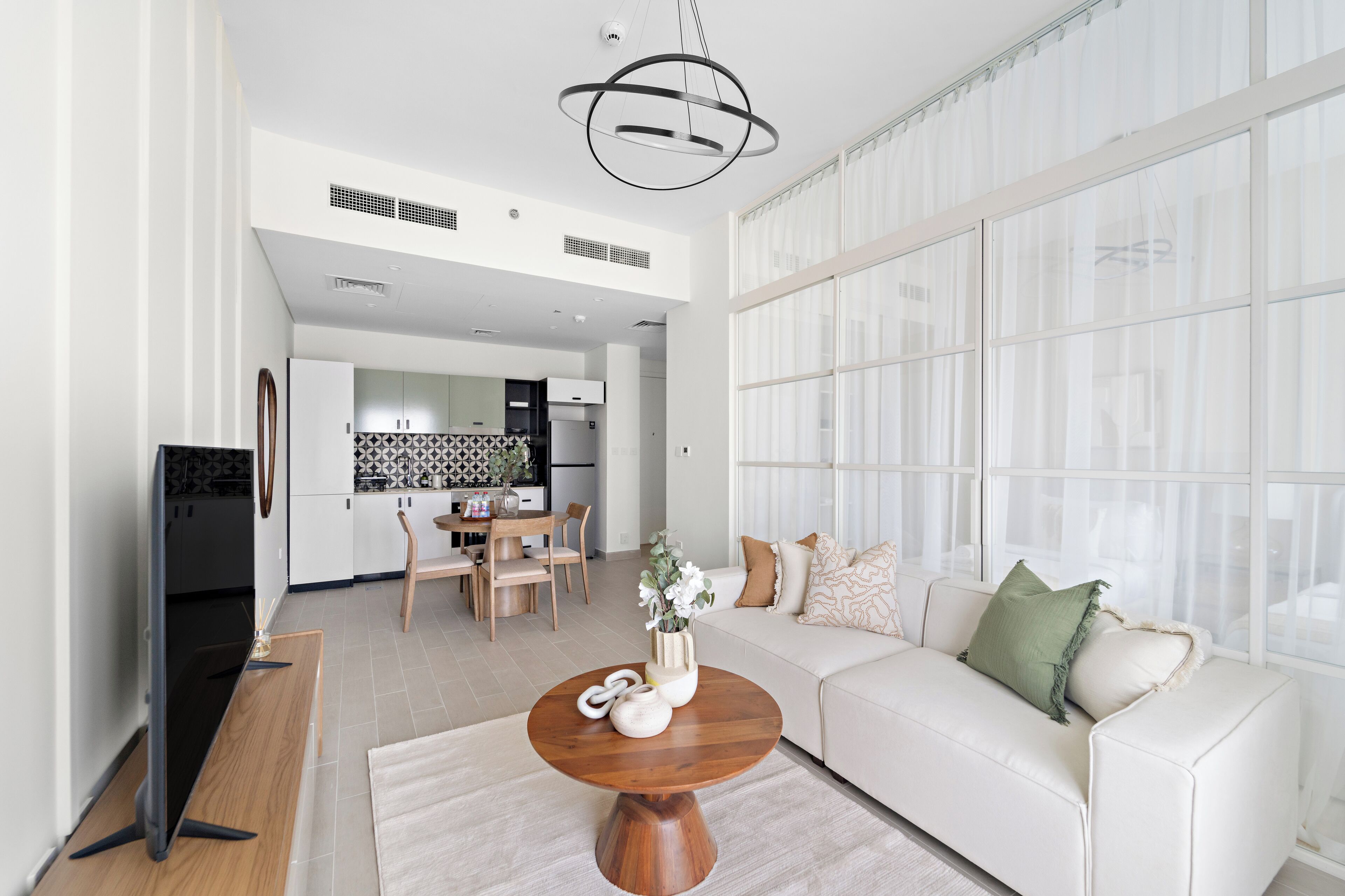 Un salon moderne avec un canapé blanc, une table basse en bois et un téléviseur posé sur un meuble.