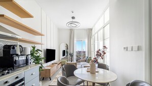 A modern kitchen with a built-in oven, microwave, and coffee maker. There is a dining area with a round table and four chairs. A large window provides a view of the city. - Silkhaus Golfville (Dubai)