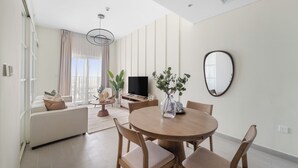 A modern living room with a sofa, dining table, chairs, a TV, and a large window with curtains. - Silkhaus Golfville (Dubai)
