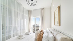 A hotel room with a large bed, white linens, a view of the city, and a modern light fixture. - Silkhaus Golfville (Dubai)