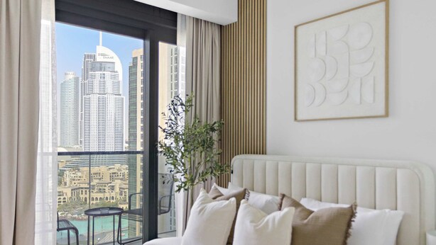A hotel room with a bed, a view of a cityscape, a plant, and a framed artwork on the wall. - Silkhaus Act One Towers (Dubai)