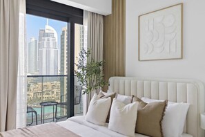 A hotel room with a bed, a view of a cityscape, a plant, and a framed artwork on the wall. - Silkhaus Act One Towers (Dubai)