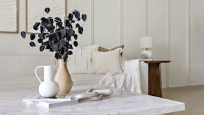 A marble table with a vase of dark leaves, a white pitcher, and a book titled "BARBERRY BAREY ART". - Silkhaus Act One Towers (Dubai)