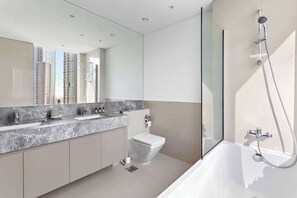 A modern bathroom with a large mirror, two sinks, a toilet, and a bathtub. - Silkhaus Act One Towers (Dubai)