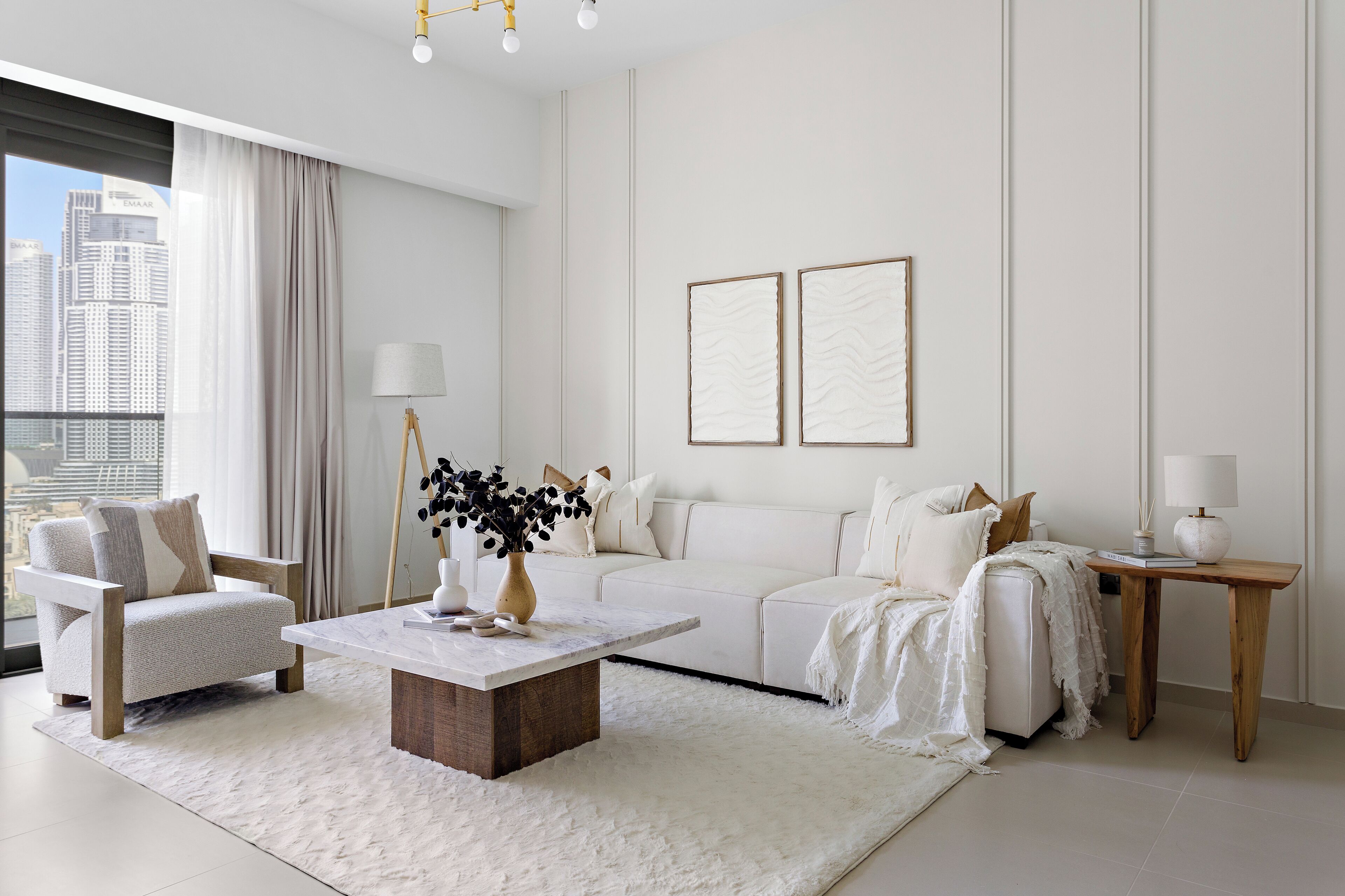 A modern living room with a white sofa, a wooden coffee table, a white armchair, and a side table with a lamp.