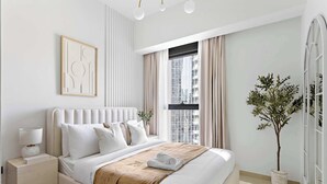 A modern bedroom with a large bed, a bedside table, a potted plant, and a window with curtains. - Silkhaus Act One Towers (Dubai)