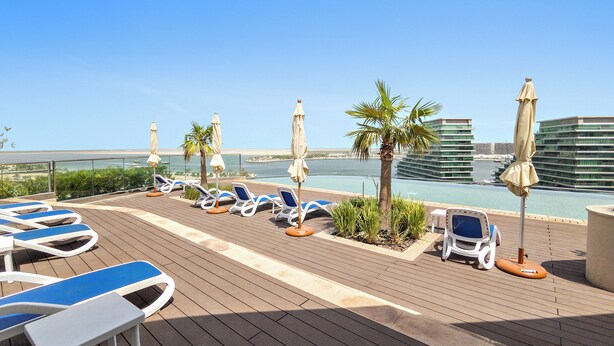 Solarium con lettini e ombrelloni affacciato su una distesa d'acqua e edifici.
