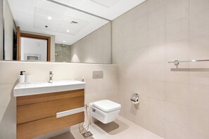 A modern bathroom with a white sink, wooden cabinet, and a toilet. - Silkhaus Al Hadeel East (Abu Dhabi)