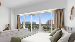 Una moderna camera d'hotel con un letto grande, un divano e vista sulla città grazie a finestre a tutta parete.