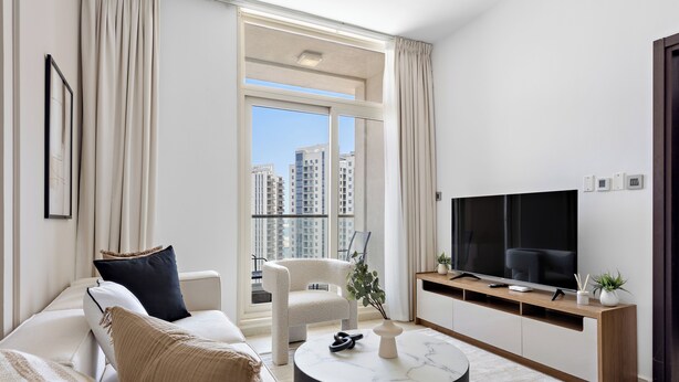 Un salon moderne comprenant un canapé, un fauteuil, une table basse, un téléviseur et un balcon offrant une vue sur la ville.