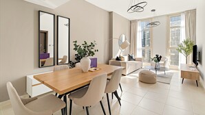 Un salon moderne avec une table à manger en bois, des chaises beiges, un canapé blanc et une grande fenêtre avec des rideaux.
