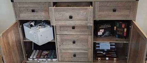 A wooden cabinet with multiple drawers and compartments, including a section with a white appliance and a section with a BINGO game.