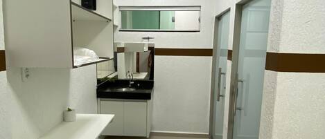 A compact hotel room with a kitchenette, a small sink, a mirror, and a bed.