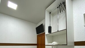 A bedroom with a bed, a small white bedside table, a mirror, a TV mounted on the wall, and a wooden door. - Pousada Torre Forte (Rio Branco)