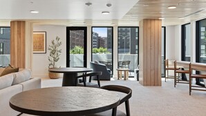 A modern lounge area with a round table, sofas, and chairs, large windows offering views of the cityscape. - VIEWS! Capitol! Year round POOL/Spa/Gym/Bowling! (Salt Lake City)