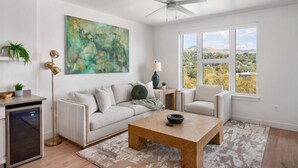 A modern living room with a sofa, a coffee table, and a view of the outdoors through large windows. - VIEWS! Capitol! Year round POOL/Spa/Gym/Bowling! (Salt Lake City)