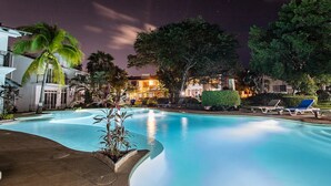A nighttime swimming pool area with lounge chairs and palm trees.