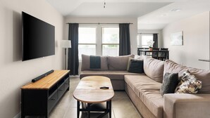Een moderne woonkamer met een flatscreen televisie, een houten salontafel, een bank en een plafondventilator.