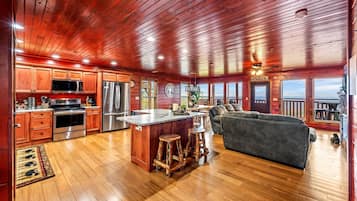 A spacious cabin with a wooden interior, a kitchen with modern appliances, a large island with stools, and a cozy seating area with a view of the outdoors.