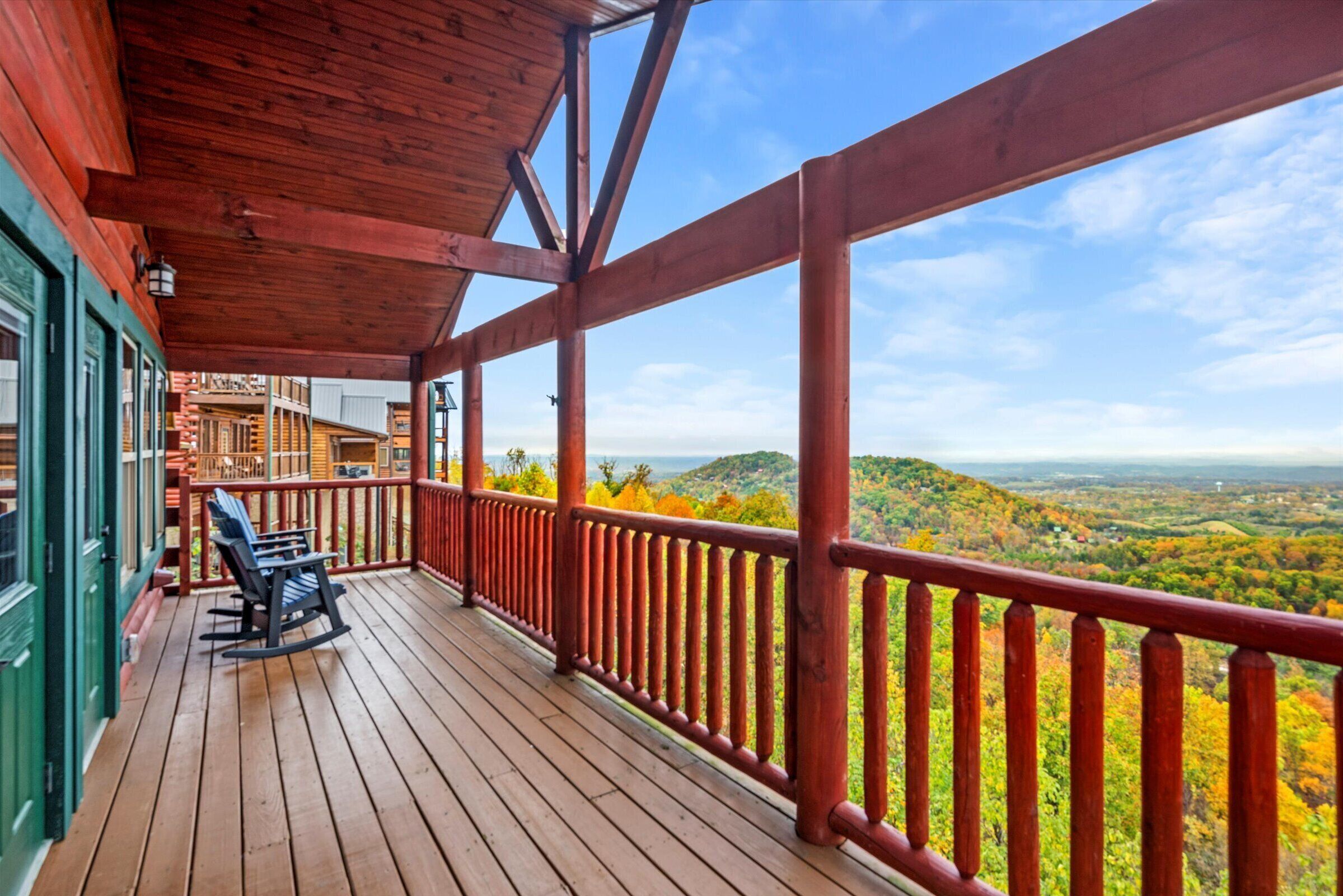 A wooden deck with a railing, a rocking chair, and a view of a valley.
