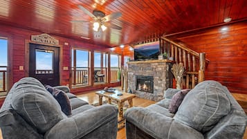 A cabin interior with a stone fireplace, wooden ceiling, and a large TV mounted on the wall.