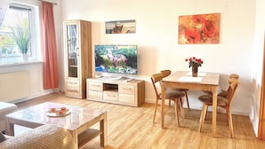 Una sala de estar con una mesa de comedor de madera, sillas, un televisor de pantalla plana, un aparador y una ventana con cortinas.
