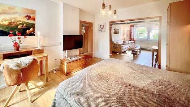 Un dormitorio moderno con una cama grande, un televisor, un escritorio con una computadora y un cuadro en la pared.