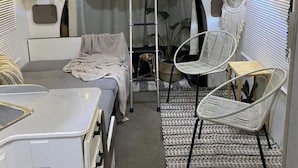 A compact RV interior with a bunk bed, a small seating area with a chair and table, and a kitchenette with a stove and cabinets. - Villa Boho Motorhome (Cabo Rojo)