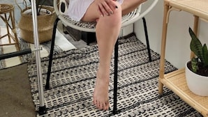 A person seated in a wicker chair with a woven pattern, holding a white mug. The room features a patterned rug, a wicker shelf, and a potted plant. - Villa Boho Motorhome (Cabo Rojo)