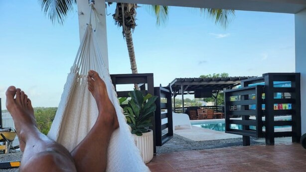 A hammock with a person's legs, a pool, a pergola, and a view of the sky. - Villa Boho Motorhome (Cabo Rojo)