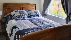 Ein Bett mit einem Holzkopfende, einer Decke mit Tiermotiven und einem Fenster mit Vorhängen.
