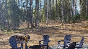 Ein Campingplatz mit Adirondack-Stühlen um ein Feuerkorb, umgeben von Kiesflächen und bewaldeter Landschaft.