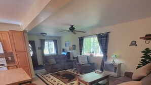 Ein geräumiges Wohnzimmer mit einer Couch, Sesseln und einem Couchtisch. Es gibt einen Essbereich mit Tisch und Stühlen sowie eine Küche mit Schränken und einer Arbeitsplatte.